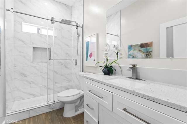 bathroom featuring wood finished floors, a stall shower, vanity, and toilet