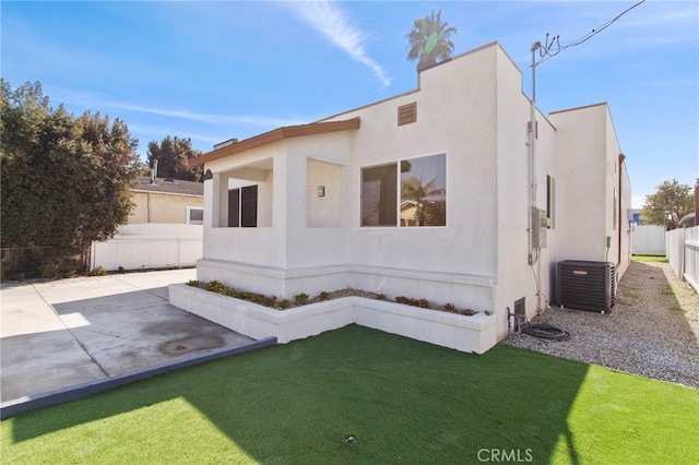 view of front of house with a patio, a fenced backyard, central AC, stucco siding, and a front yard