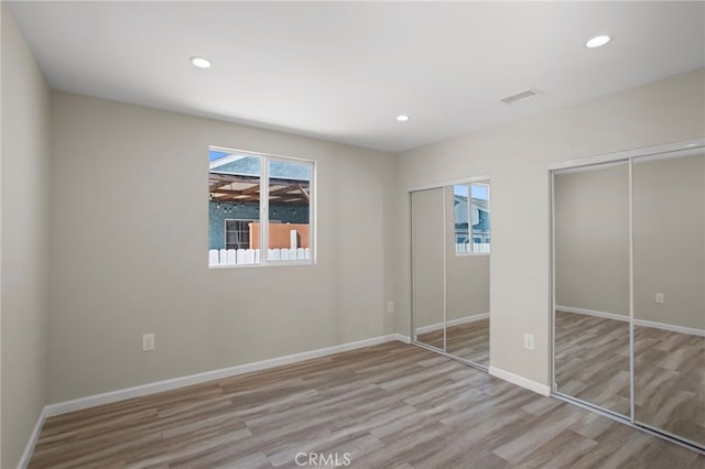 unfurnished bedroom featuring baseboards, recessed lighting, wood finished floors, and multiple closets