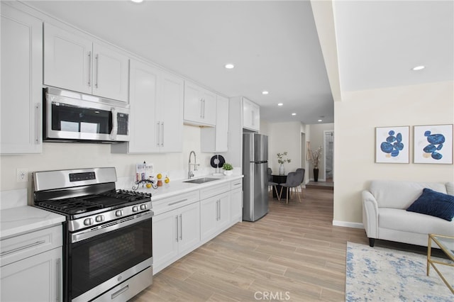 kitchen with light wood-style flooring, appliances with stainless steel finishes, open floor plan, white cabinetry, and a sink