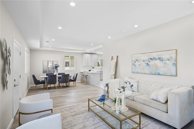 living area with light wood-style flooring, recessed lighting, visible vents, baseboards, and a raised ceiling