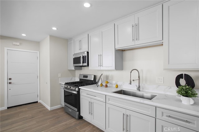 kitchen with recessed lighting, wood finished floors, a sink, white cabinetry, and appliances with stainless steel finishes