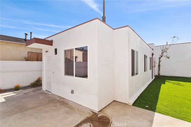 exterior space with a patio area, fence, a lawn, and stucco siding