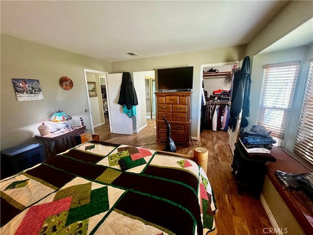 bedroom with wood finished floors, visible vents, baseboards, a closet, and a walk in closet