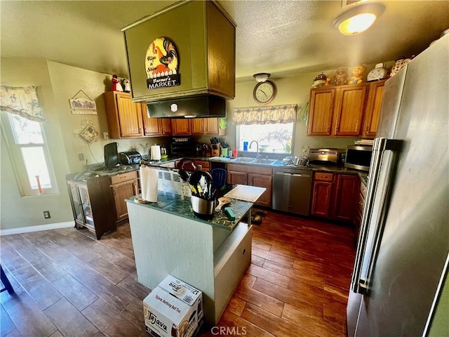 kitchen with stainless steel appliances, dark wood-style flooring, a sink, a center island, and dark countertops