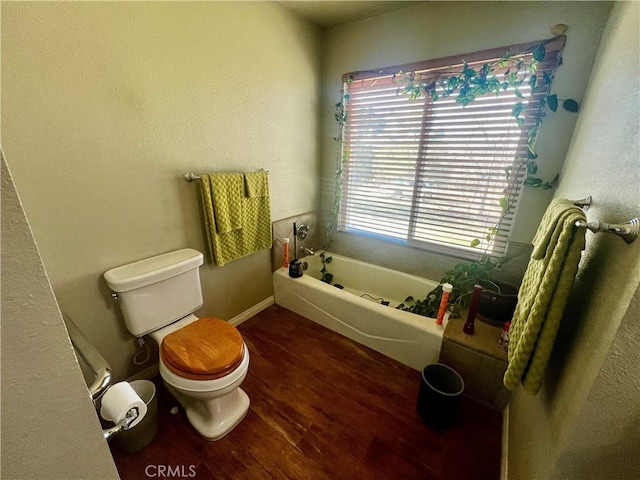 full bathroom with toilet, baseboards, wood finished floors, and a bath