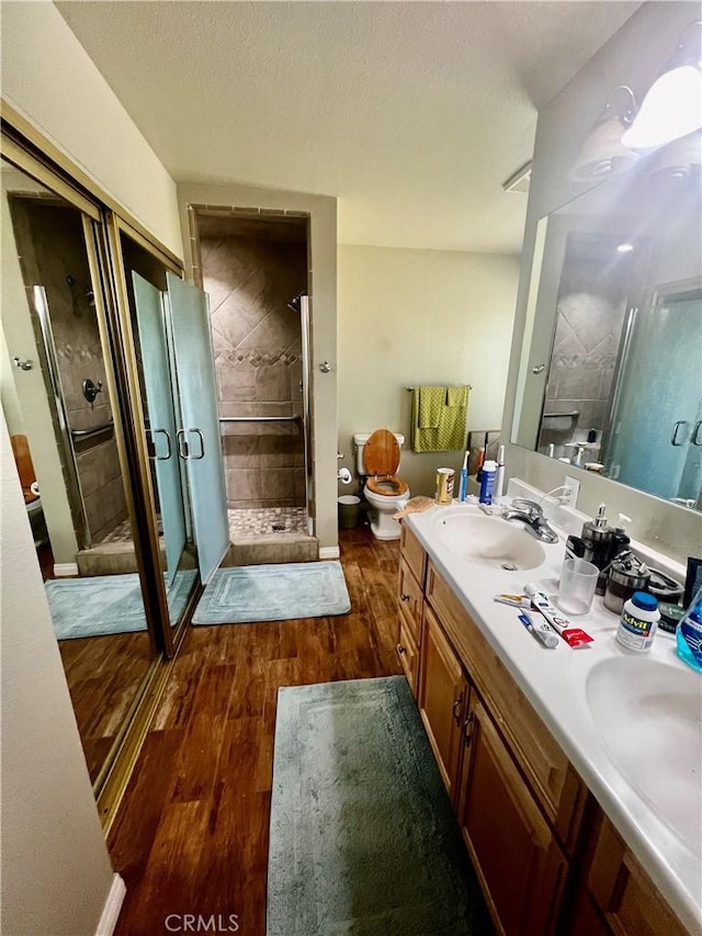 full bathroom with a stall shower, toilet, wood finished floors, a textured ceiling, and a sink