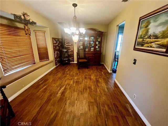 unfurnished dining area with visible vents, a wood stove, wood finished floors, a chandelier, and baseboards