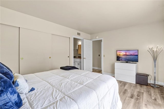 bedroom with baseboards, visible vents, ensuite bathroom, light wood-type flooring, and a closet