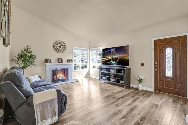 living area with lofted ceiling, a brick fireplace, wood finished floors, and baseboards