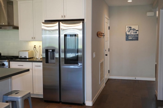 kitchen with dark countertops, wall chimney range hood, stainless steel refrigerator with ice dispenser, and white cabinetry