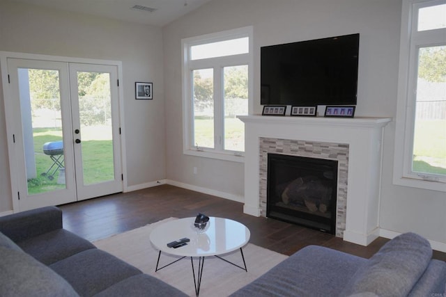 living area featuring french doors, lofted ceiling, visible vents, a tiled fireplace, and dark wood-type flooring