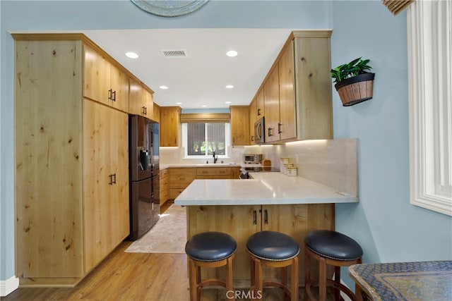 kitchen with visible vents, a peninsula, stainless steel microwave, light wood-type flooring, and black refrigerator with ice dispenser