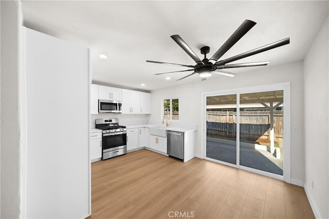 kitchen featuring stainless steel appliances, a sink, white cabinetry, light countertops, and light wood-type flooring