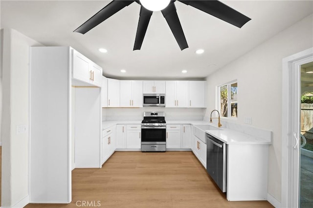 kitchen with appliances with stainless steel finishes, light wood-style floors, white cabinetry, a sink, and recessed lighting