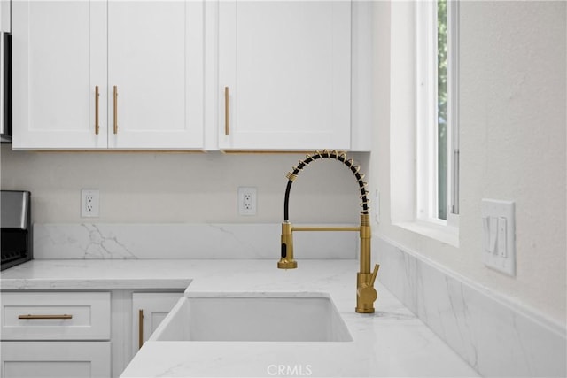 room details featuring light stone counters, white cabinets, and a sink