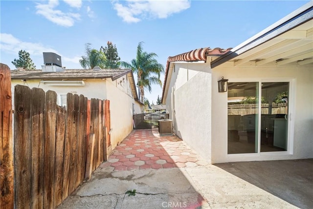 view of property exterior with a gate, fence, central air condition unit, a patio area, and stucco siding