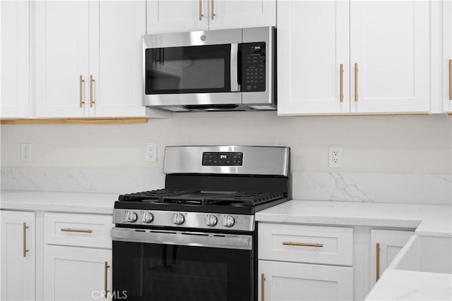 kitchen with stainless steel appliances, light stone countertops, and white cabinets