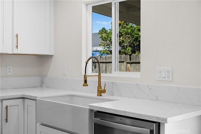 kitchen with light stone counters, white cabinets, a sink, and stainless steel dishwasher