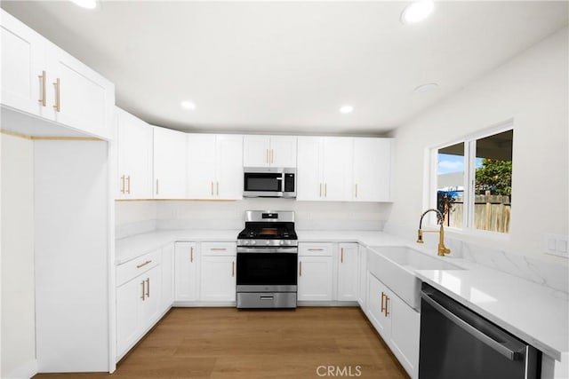 kitchen featuring light wood finished floors, recessed lighting, appliances with stainless steel finishes, white cabinetry, and a sink