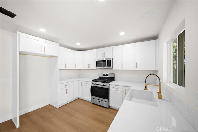 kitchen featuring stainless steel appliances, light countertops, light wood-type flooring, white cabinetry, and a sink