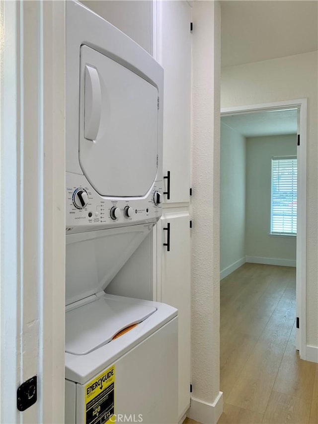 clothes washing area with light wood finished floors, stacked washer and dryer, baseboards, and laundry area