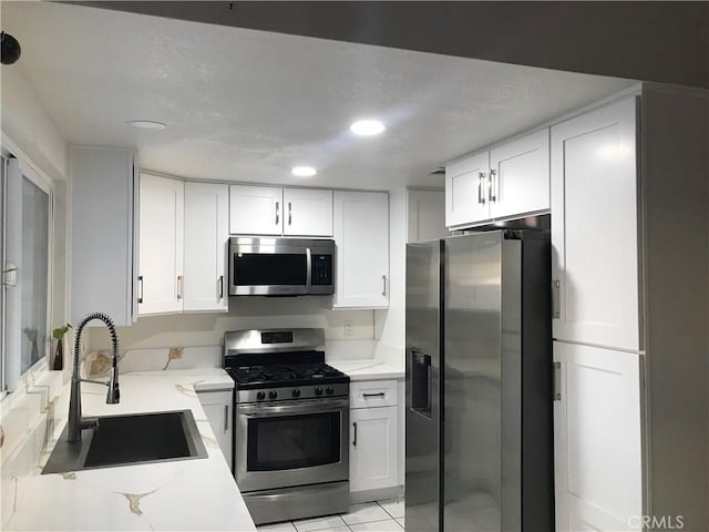 kitchen featuring stainless steel appliances, white cabinetry, a sink, and light stone counters