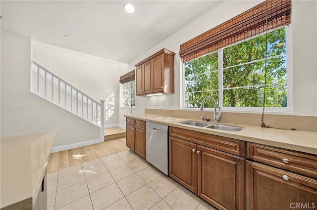 kitchen with a sink, brown cabinets, light countertops, and stainless steel dishwasher