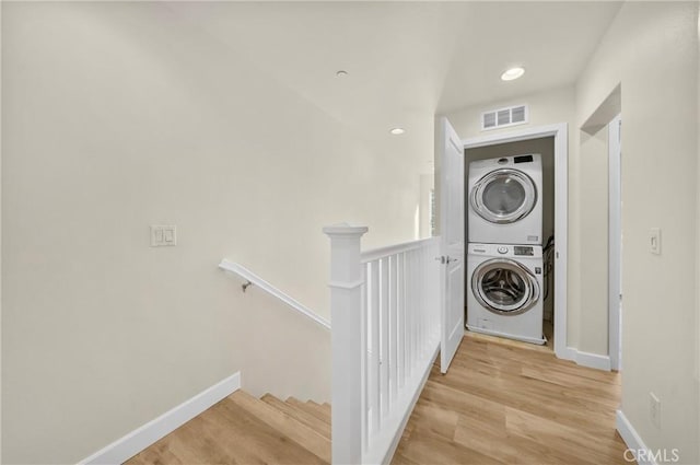 laundry room with laundry area, visible vents, baseboards, stacked washer / dryer, and light wood-style flooring