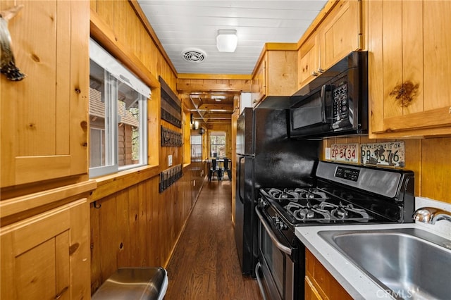 kitchen featuring wooden walls, gas range, black microwave, and a sink