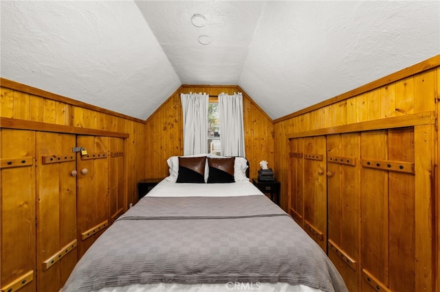 bedroom with a closet, wooden walls, a textured ceiling, and lofted ceiling