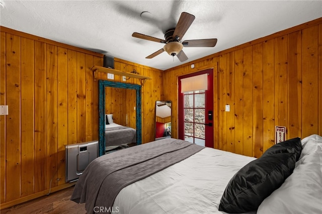 bedroom featuring a ceiling fan, a textured ceiling, wood finished floors, and wooden walls