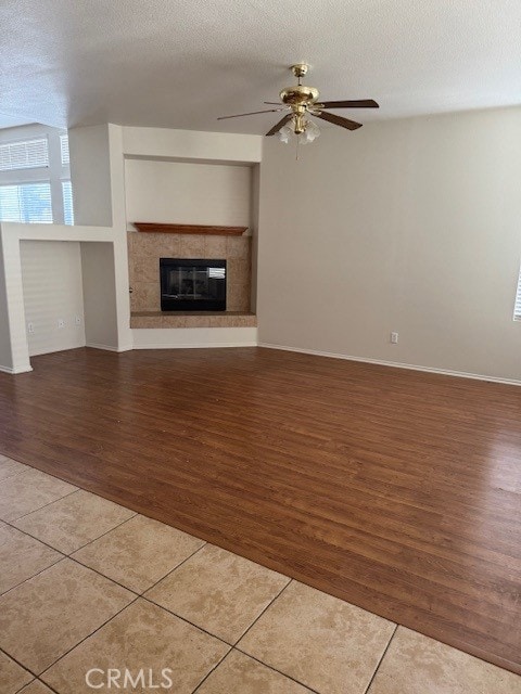 unfurnished living room featuring a textured ceiling, a tile fireplace, a ceiling fan, and tile patterned floors