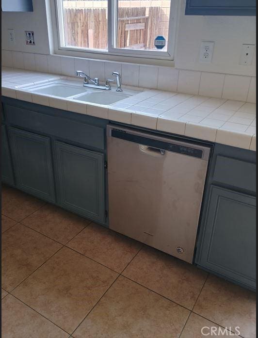 kitchen featuring tile counters, light tile patterned flooring, a sink, and stainless steel dishwasher