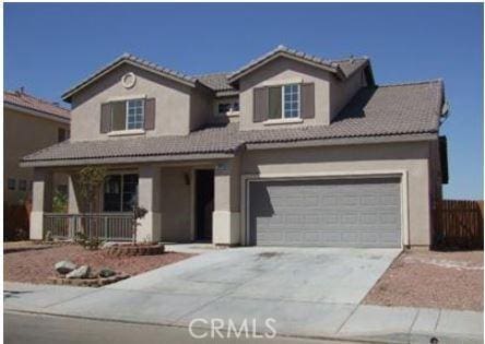 traditional-style home with a tile roof, stucco siding, a porch, concrete driveway, and a garage