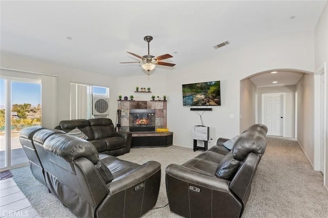 living area with arched walkways, a tile fireplace, light carpet, visible vents, and a ceiling fan