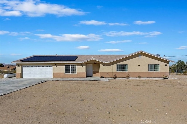 ranch-style home featuring driveway, solar panels, a tiled roof, an attached garage, and stucco siding