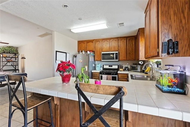 kitchen featuring stainless steel appliances, visible vents, a sink, and tile countertops