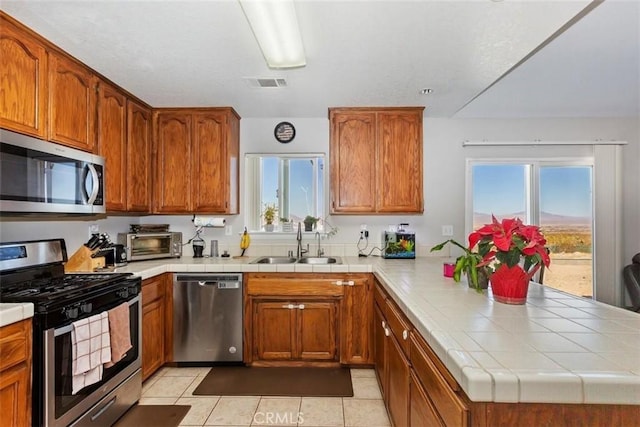 kitchen with visible vents, appliances with stainless steel finishes, brown cabinets, a peninsula, and a sink