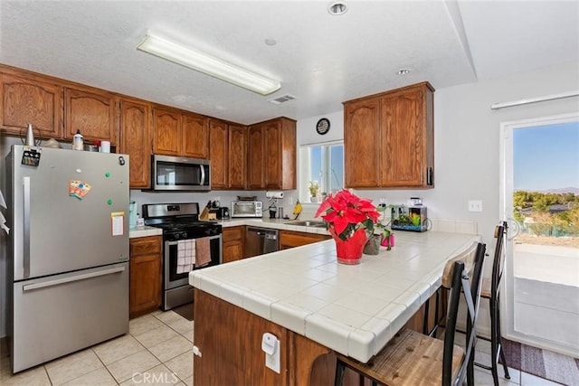 kitchen with appliances with stainless steel finishes, brown cabinets, plenty of natural light, and a peninsula