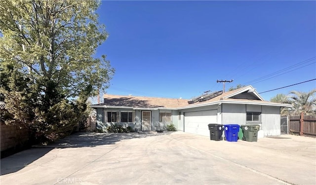 ranch-style house with a garage, fence, solar panels, and concrete driveway