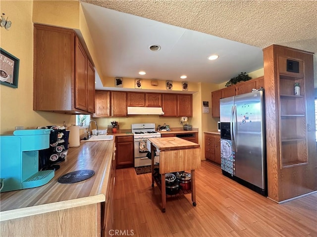 kitchen featuring under cabinet range hood, a sink, wood counters, white range with gas cooktop, and stainless steel refrigerator with ice dispenser