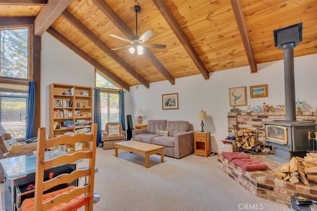 living area featuring a wood stove, a wealth of natural light, beamed ceiling, and light colored carpet