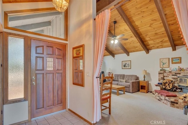 foyer with lofted ceiling with beams, wooden ceiling, light carpet, a ceiling fan, and a wood stove