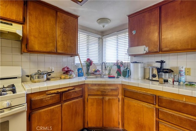 kitchen featuring tile countertops, under cabinet range hood, white range with gas cooktop, and decorative backsplash