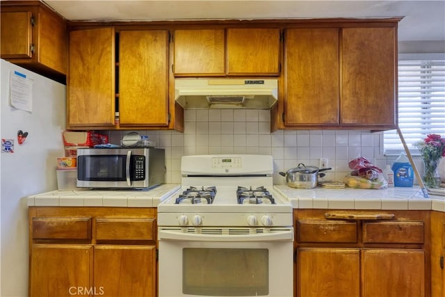 kitchen featuring tile countertops, white appliances, decorative backsplash, and under cabinet range hood