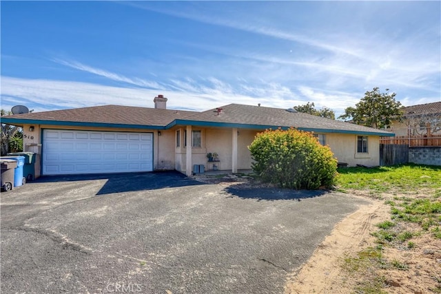 ranch-style home featuring an attached garage, fence, aphalt driveway, and stucco siding