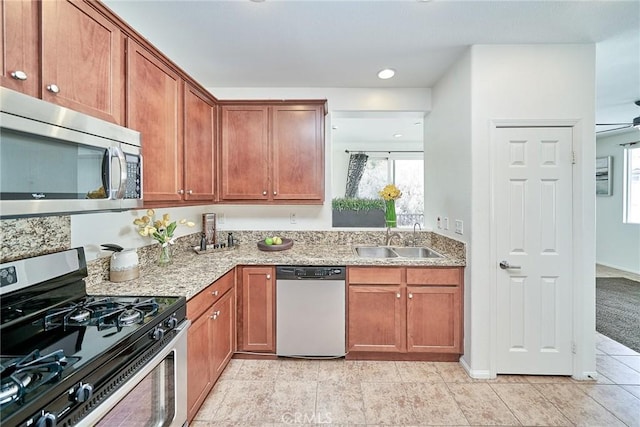 kitchen with appliances with stainless steel finishes, a sink, light stone countertops, and brown cabinets