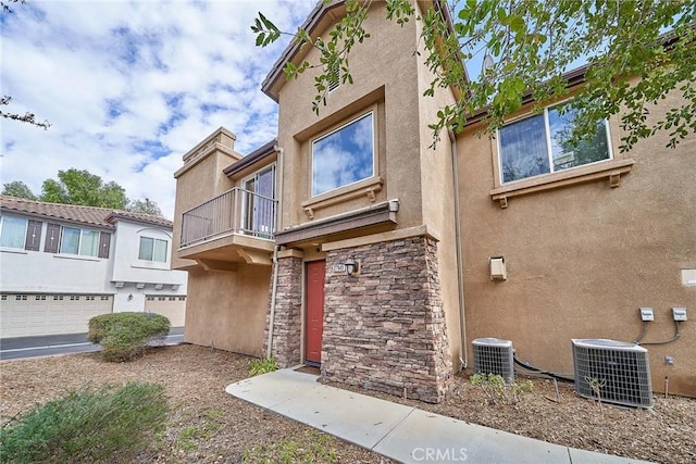 view of front of property featuring stone siding, stucco siding, a balcony, and central AC unit