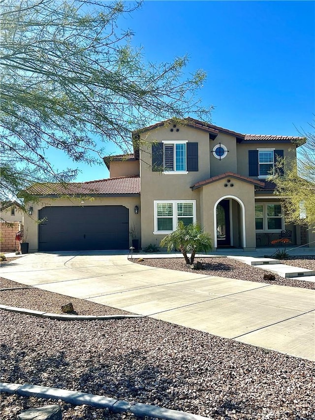 mediterranean / spanish house with a garage, concrete driveway, a tiled roof, and stucco siding